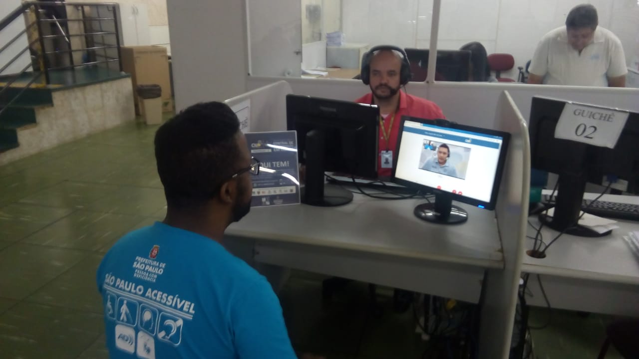 Foto mostra tela do computador com imagem de atendimento em LIBRAS e cidadão sendo orientado pelo computador